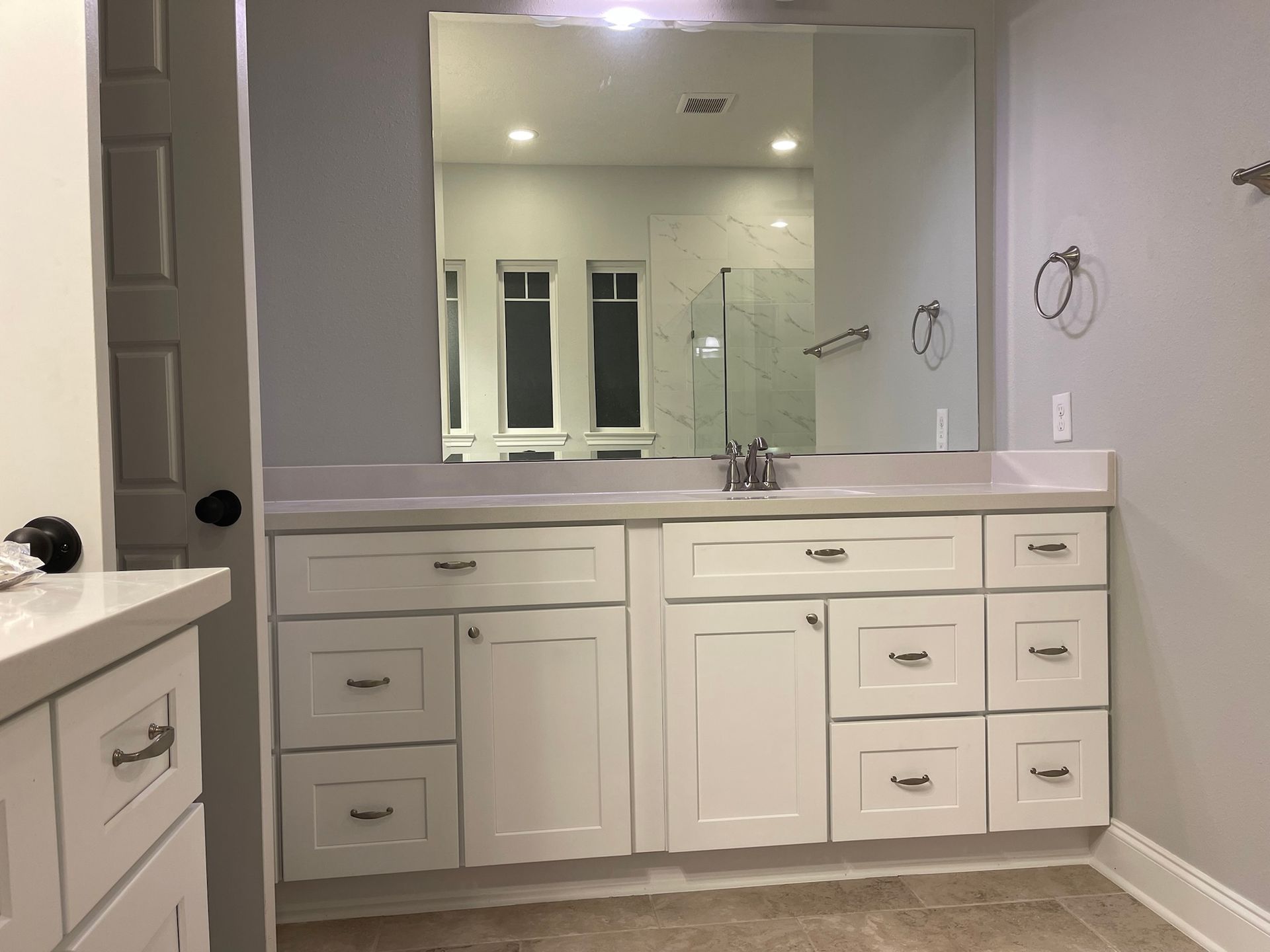 A bathroom with white cabinets , drawers and a large mirror.
